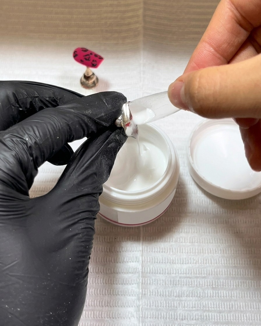 A brush applying a thin layer of black gel base coat to a fresh nail tip.