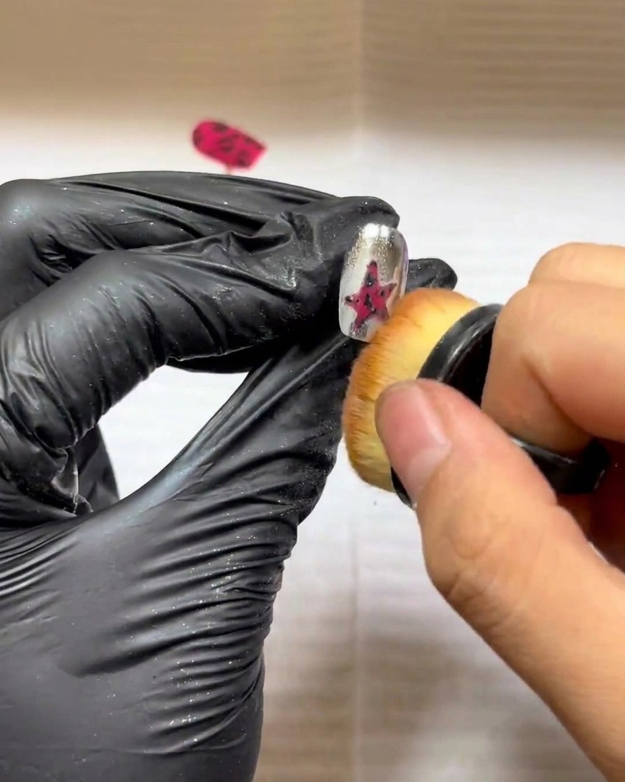 A small makeup brush being used to gently sweep excess powder from a textured star nail art design.