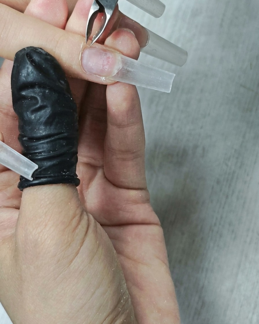 A close-up view of a metal cuticle bit being used to clean around the cuticle area of a fingernail.