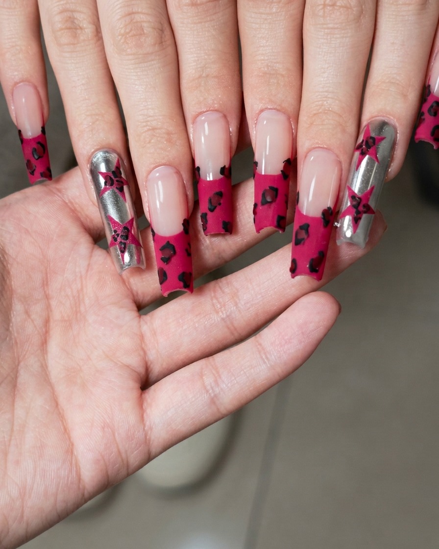 A close-up view of a fine nail art brush painting a small black star on a metallic silver nail surface.