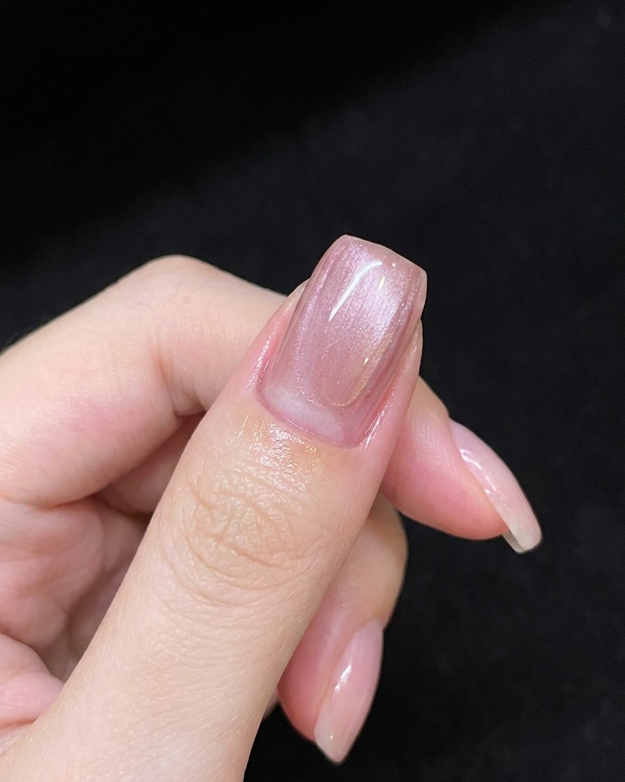 A hand holding a magnetic wand over a pink gel-coated nail to create a diagonal shimmer line.
