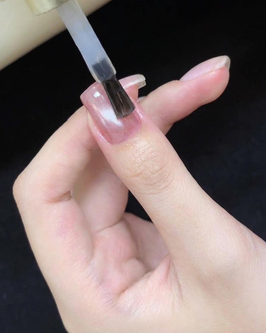 A brush applying a clear, glossy top coat over the cured cat eye nail design.