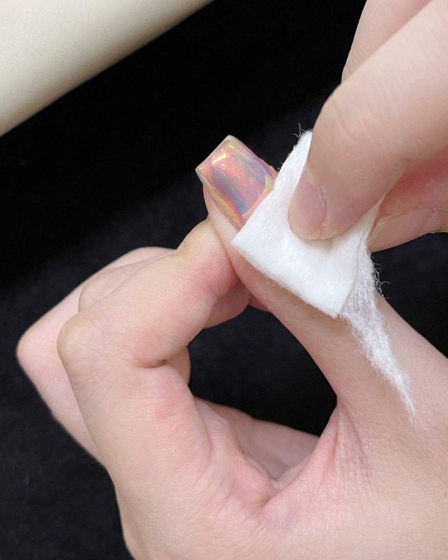 A foam eyeshadow applicator rubbing iridescent powder onto a smooth, glossy nail surface.