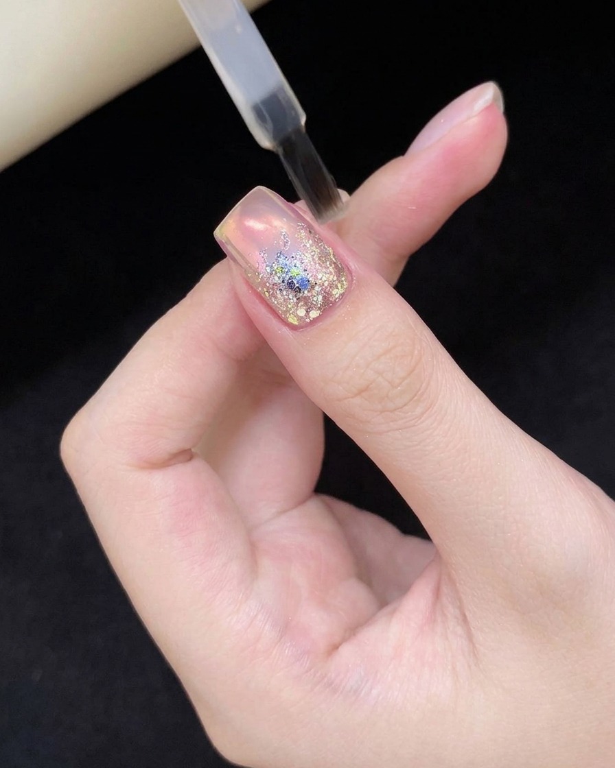 A fingernail with glitter nail art being held inside a professional UV/LED nail curing lamp.