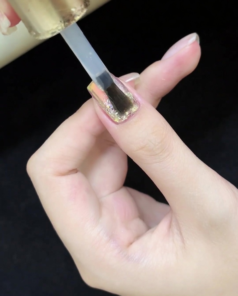 A brush applying a clear, glossy top coat over the completed glitter and cat-eye nail design.