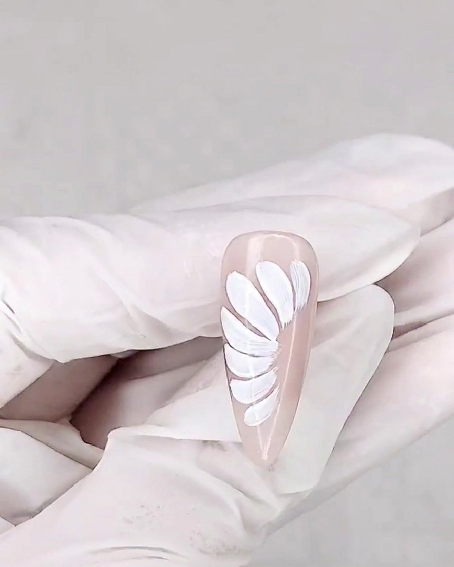 A brush applying a matte top coat over the daisy-painted nail.