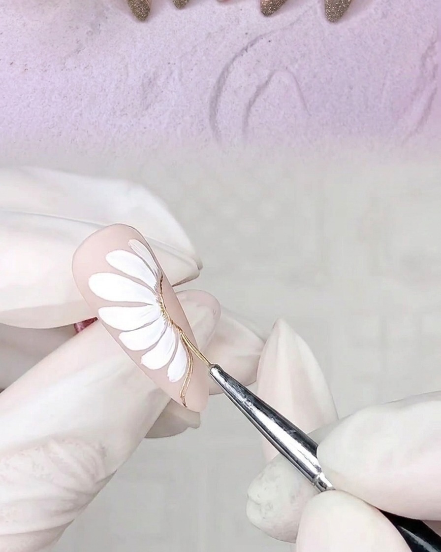 A hand with a decorated nail placed inside a UV nail lamp to cure the freshly applied gel adhesive outlines.