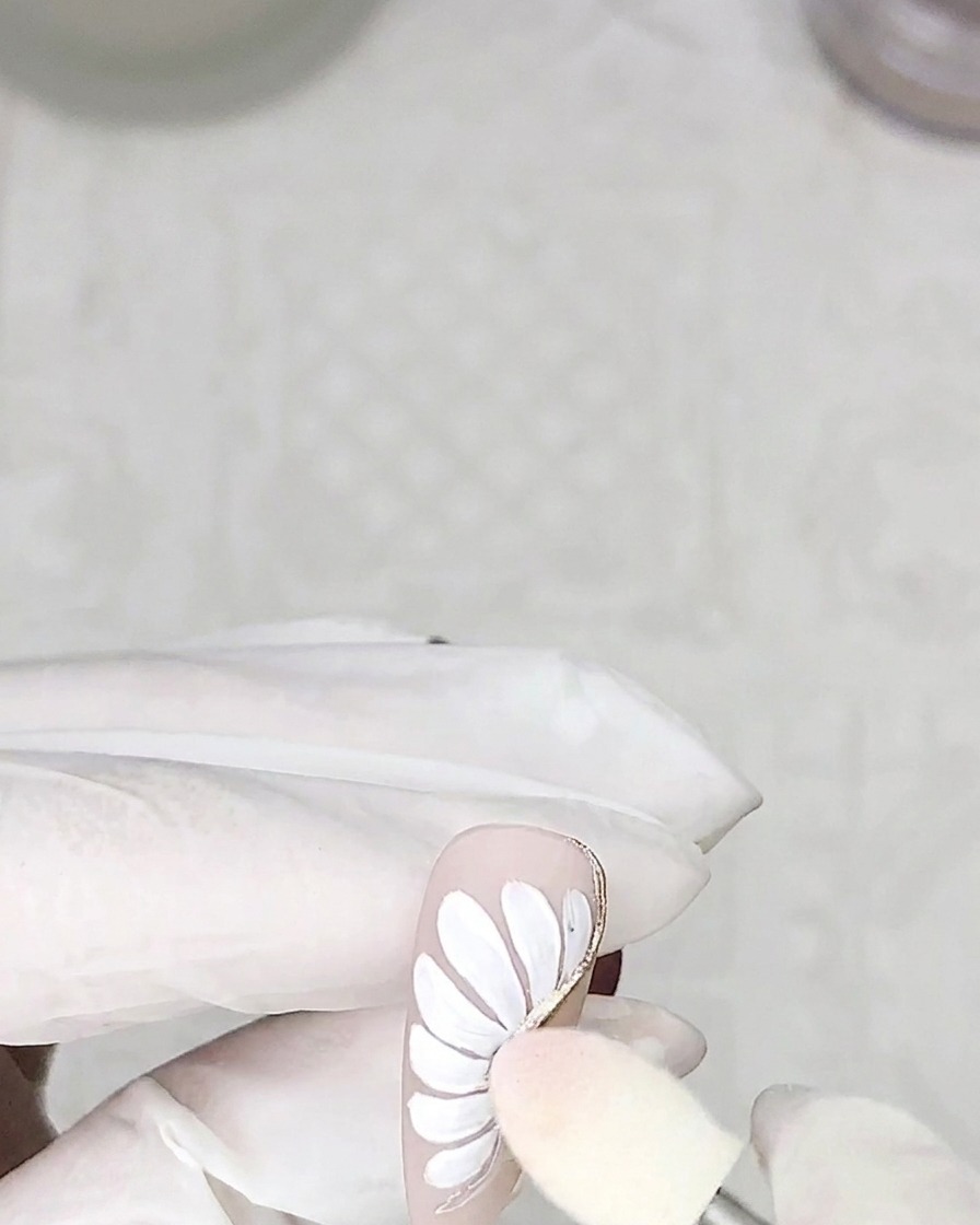 A sponge applicator dabbing silver chrome powder onto the cured adhesive petal outlines on a nail.