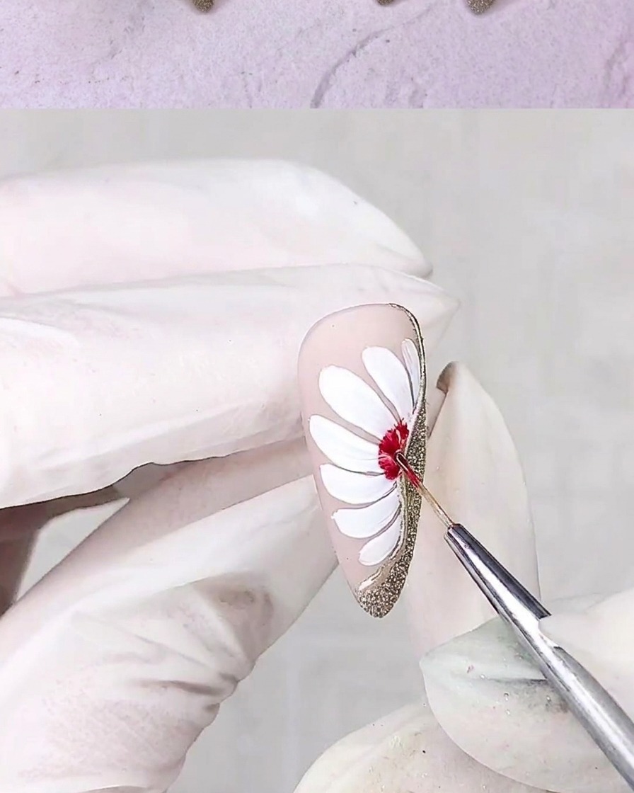 A fine detail brush applying red gel to the center of a white daisy design on a nail.