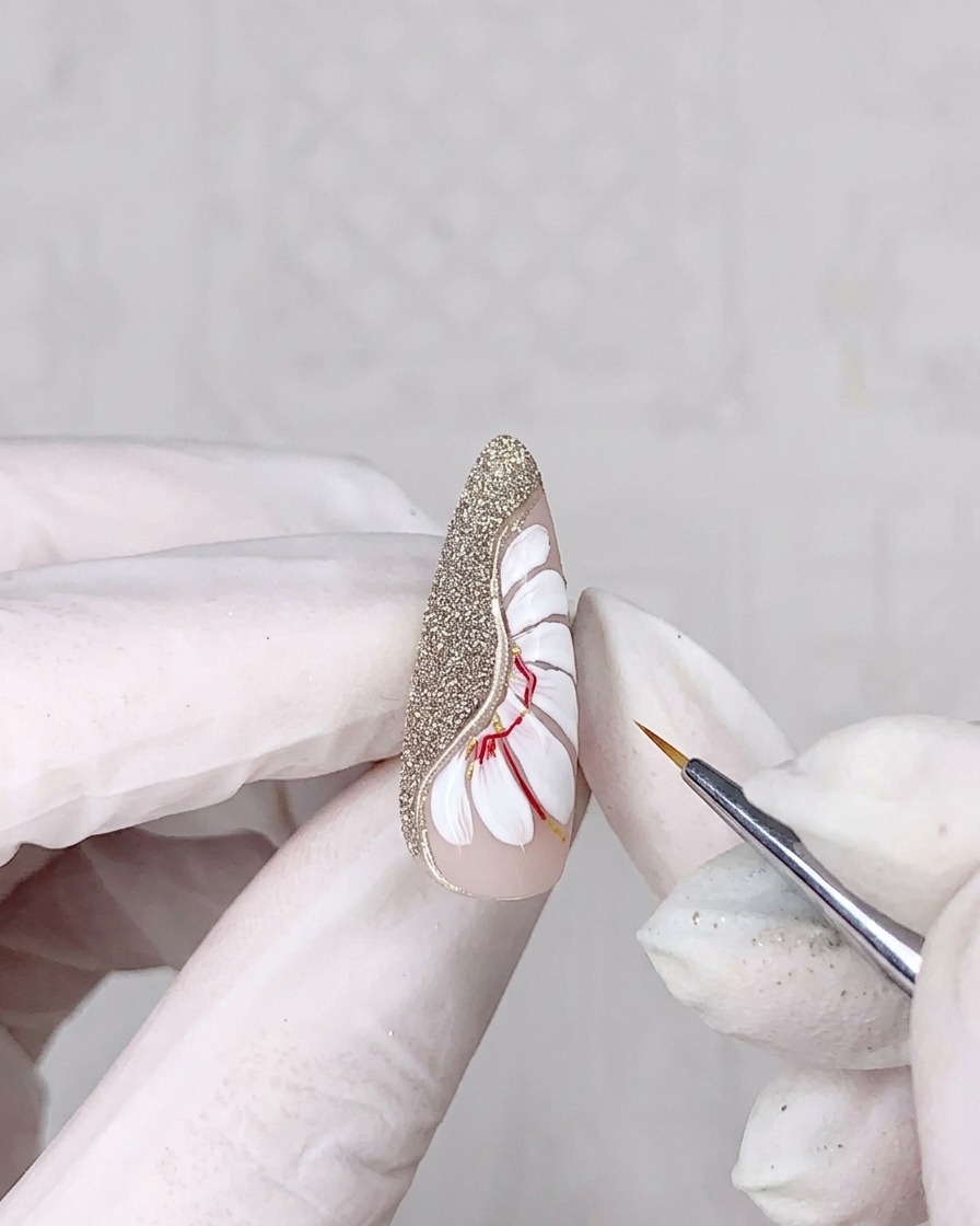 A close-up view of a hand using a thin liner brush to add fine lines onto white painted daisy petals.