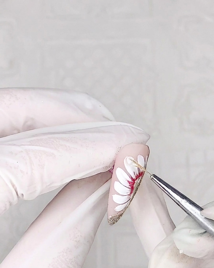 A close-up of a liner brush applying a clear, thick adhesive gel onto the surface of a daisy petal.