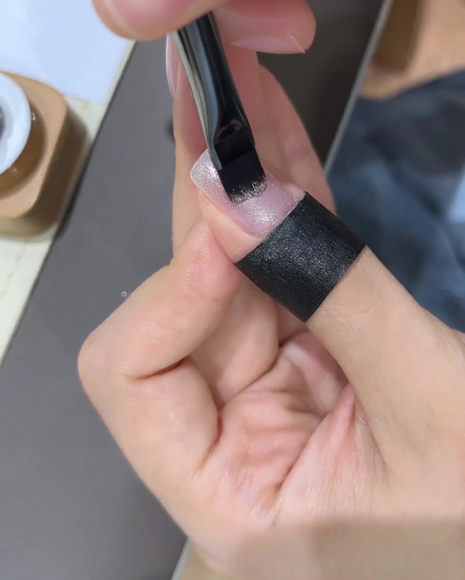 A hand using a nail magnet over a freshly painted gel nail to manipulate the glitter particles.