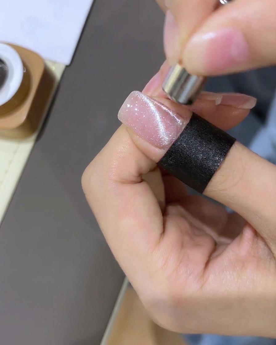 A close-up showing a magnet being used to pull magnetic glitter into a concentrated, spherical shape on the nail.