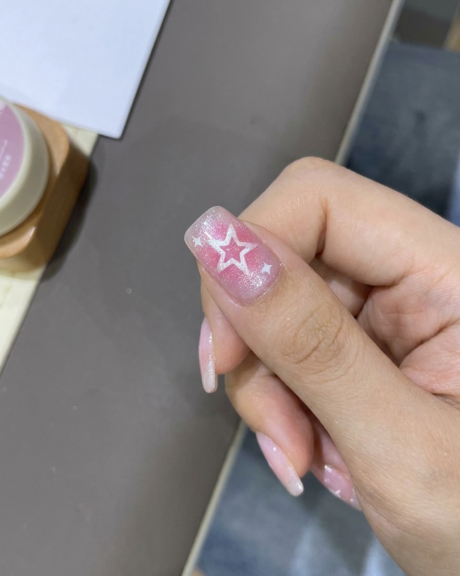 A fine liner brush adding thin white highlights around the star designs on the nail.
