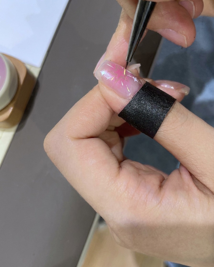 A dotting tool being used to place small, colorful accents around the star-decorated nail.