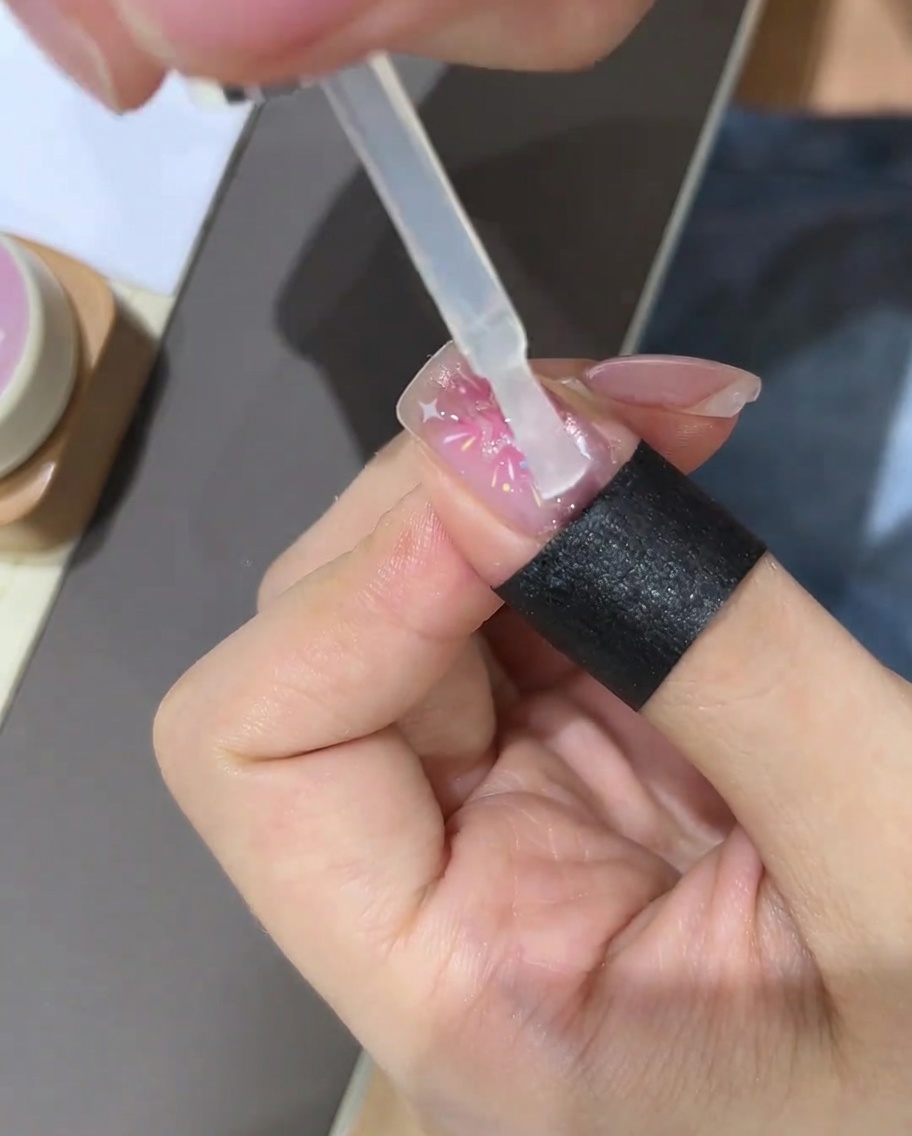 A brush applying a clear top coat over the completed star nail design.