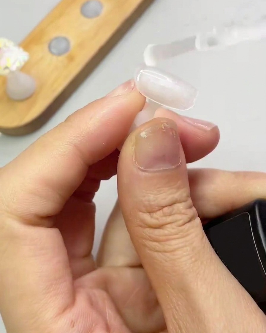 A brush applying a clear, thin layer of reinforcement gel to a nail tip.