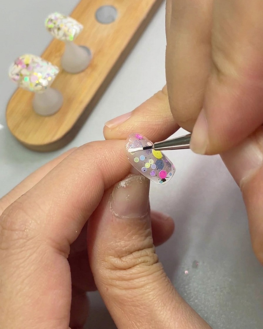 A fine detail brush applying white sculpting gel to create a petal shape on a nail.