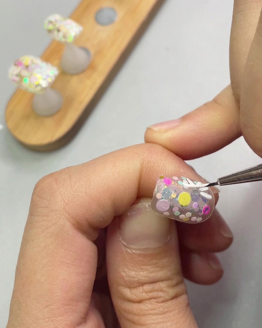 A fine detail brush adding more white petals to form a daisy shape on the nail.