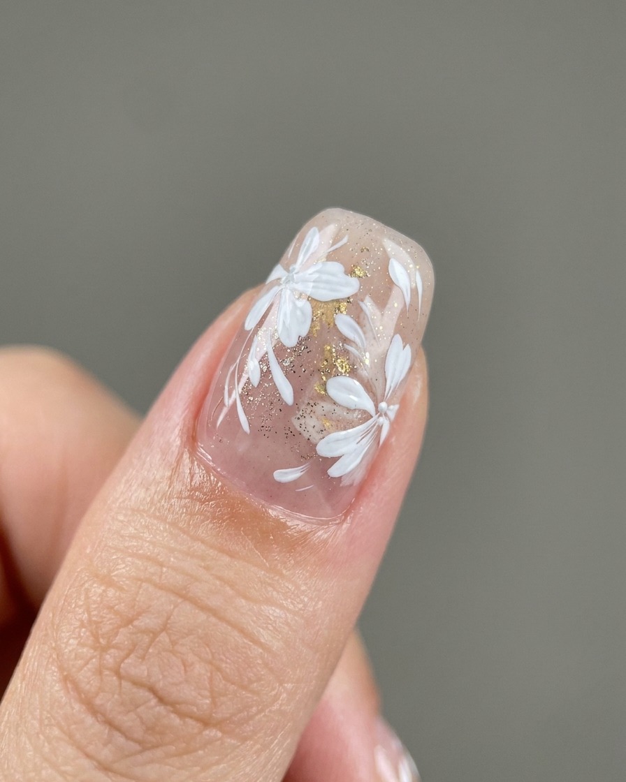 A detail brush placing flecks of gold foil onto a nail.