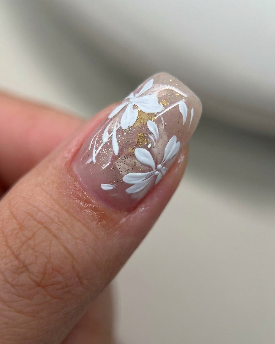 A close-up of a nail with a sheer nude-pink tint being coated with a thin layer of fine gold glitter using a gel brush.