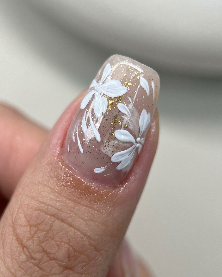 A brush applying clear top coat over a nail decorated with floral art and gold accents.