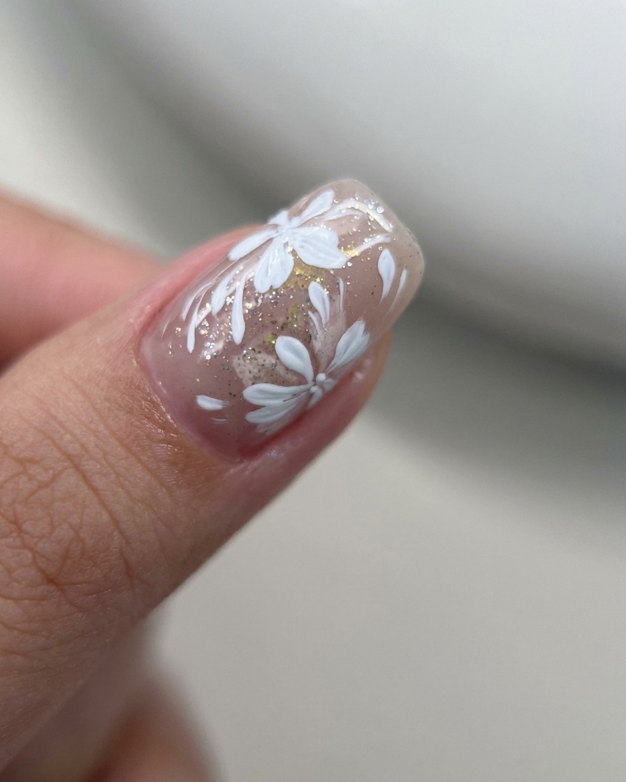 Close-up of a liner brush adding small, white petals to an existing floral design on a nude gel nail.