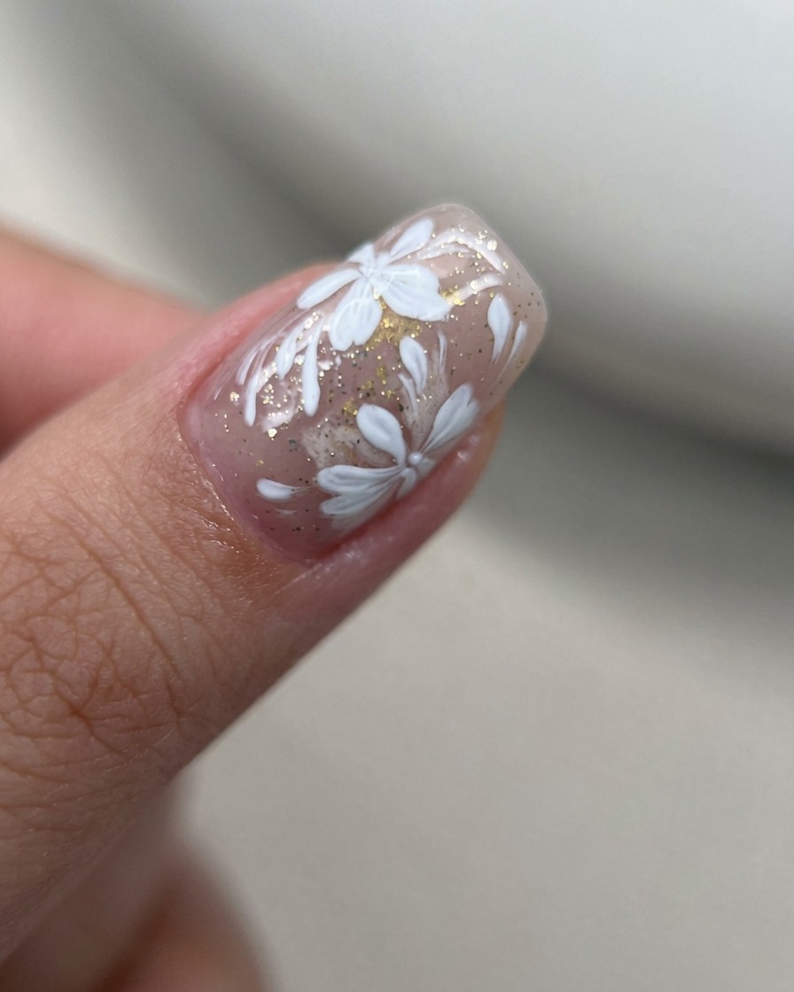 A macro shot of white gel flower petals being painted in a tight, concentrated cluster on a nude nail surface.