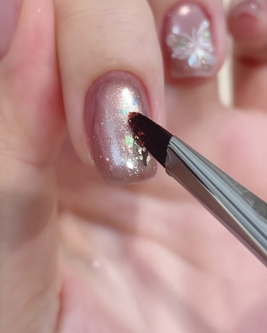 A nail art brush depositing a small dot of white gel paint to serve as the starting point for a floral design.