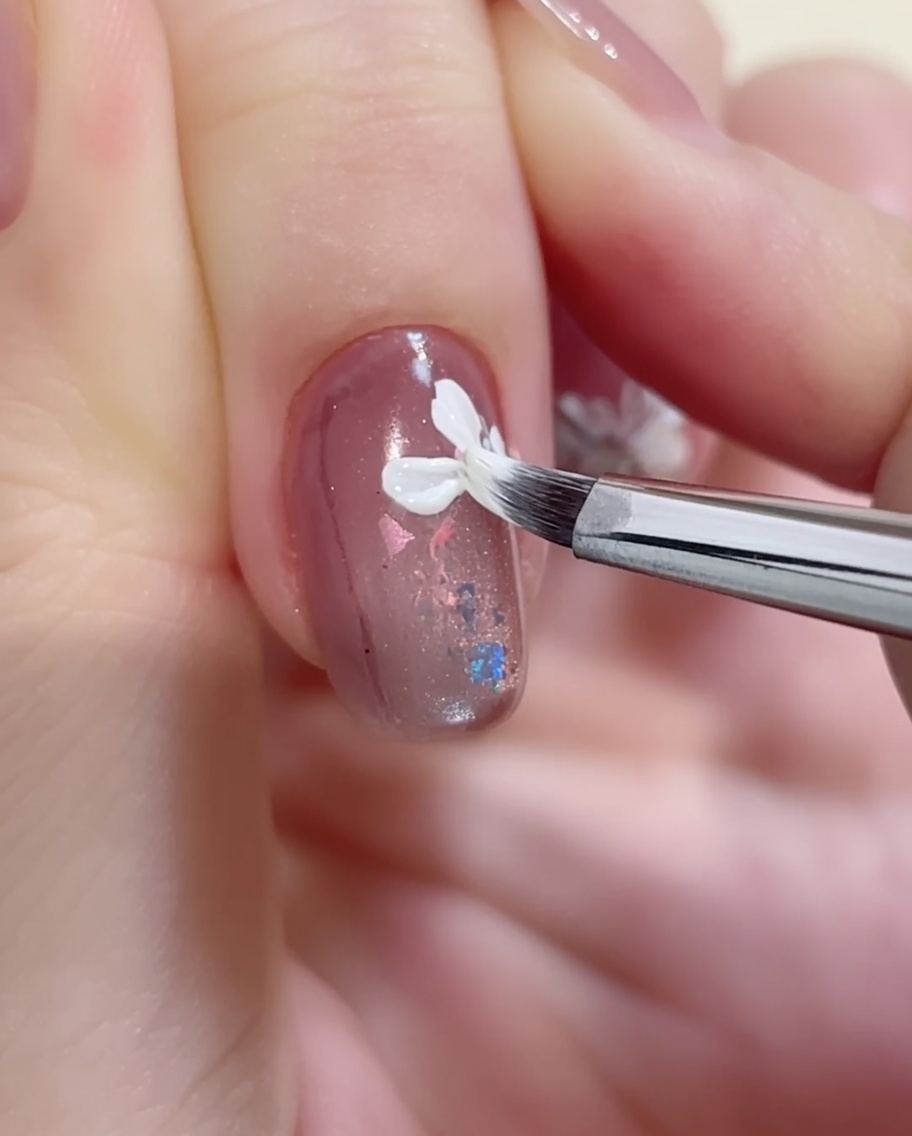 A fine-tipped brush carefully drawing delicate, irregular white petals on a nail surface.