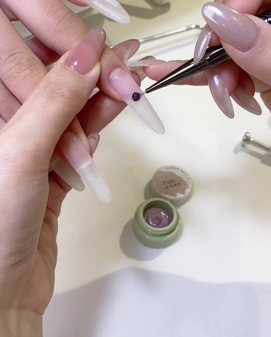 A gel brush applying a smooth coat of nude gel polish to the surface of a nail.