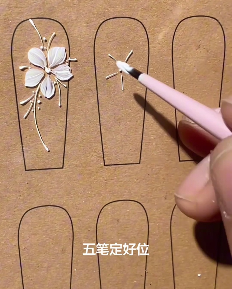 A flat brush applying a thick white gel petal on a nail, pulling from the outer edge toward the center.