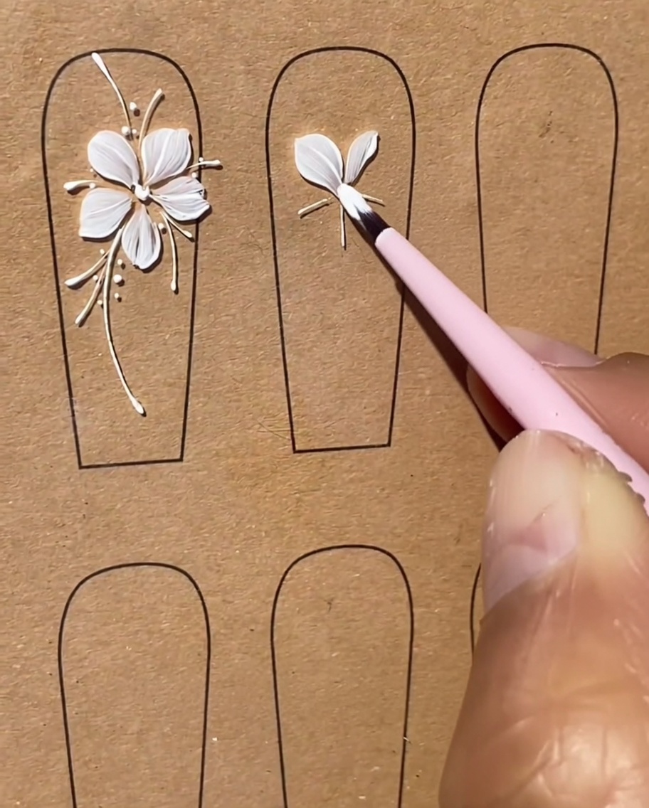 A brush carefully shaping a third white gel petal as part of the five-petal flower design.