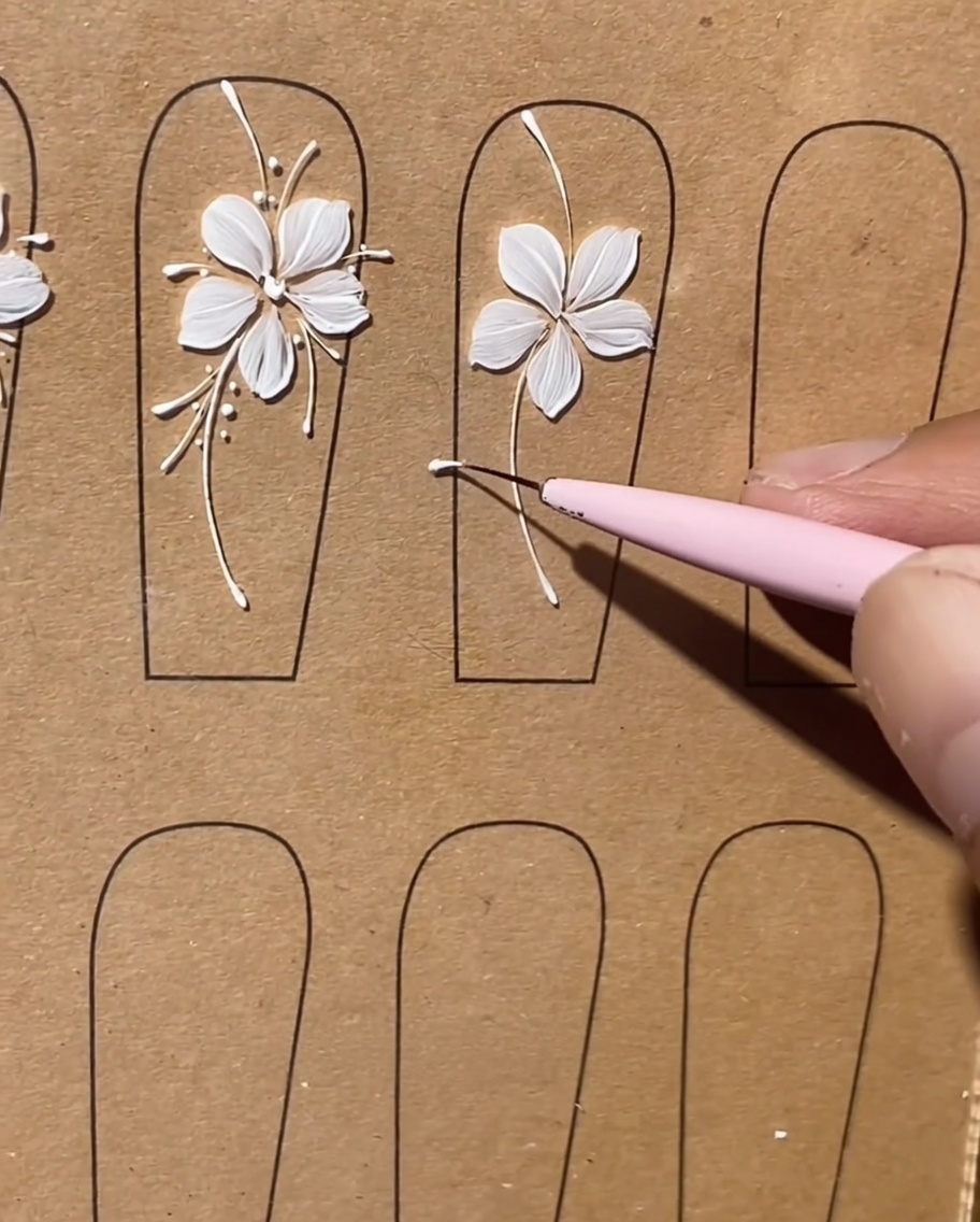 Close-up showing a liner brush adding long, delicate white lines between the petals of a painted flower.
