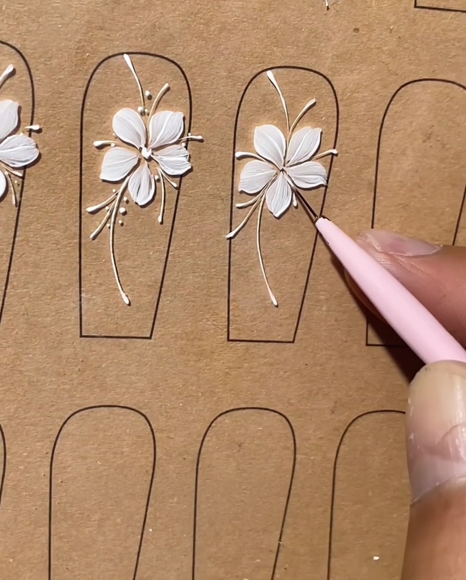 A detail shot showing small white dots being applied as highlights along the lines of a floral nail design.