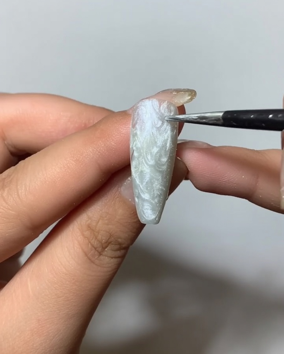 A brush applying a clear matte top coat over a textured silver spider gel nail surface.