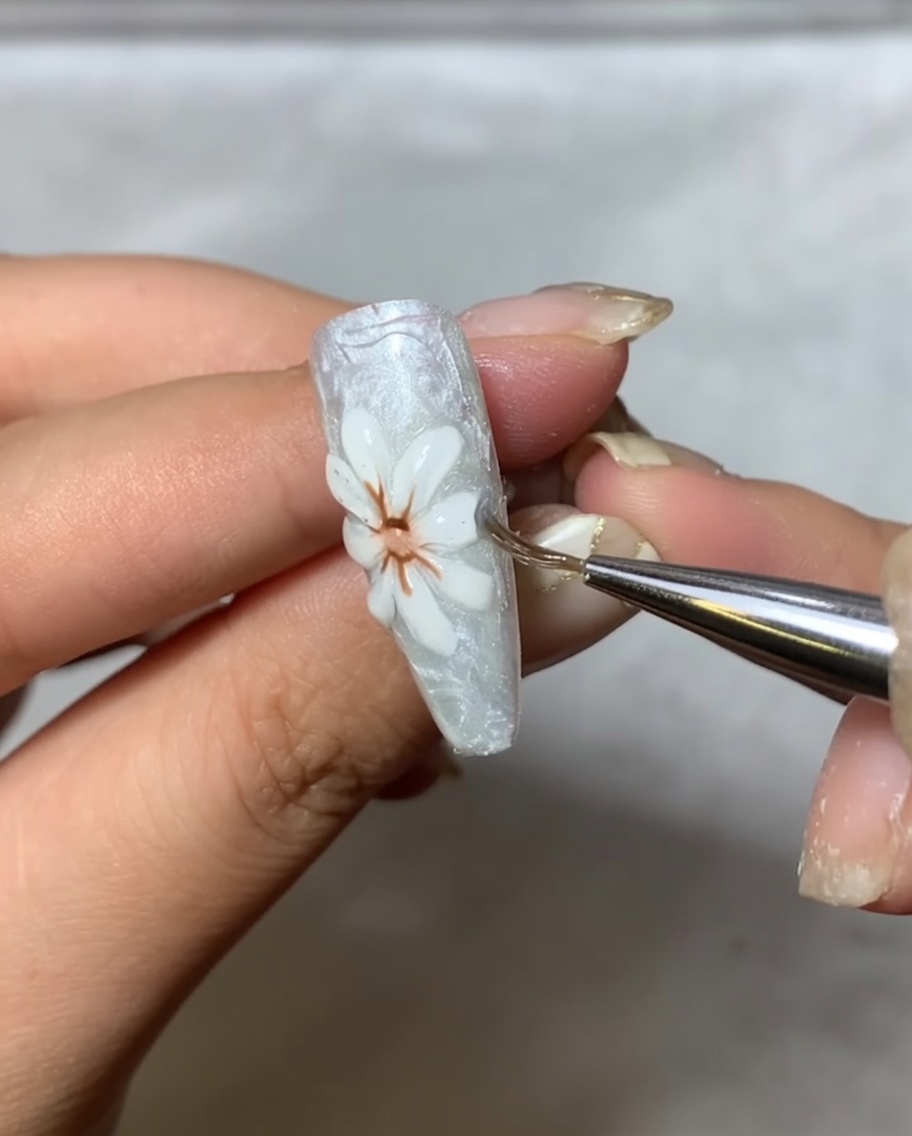 An applicator brush gently buffing metallic mirror powder onto the raised white petals of the nail art.