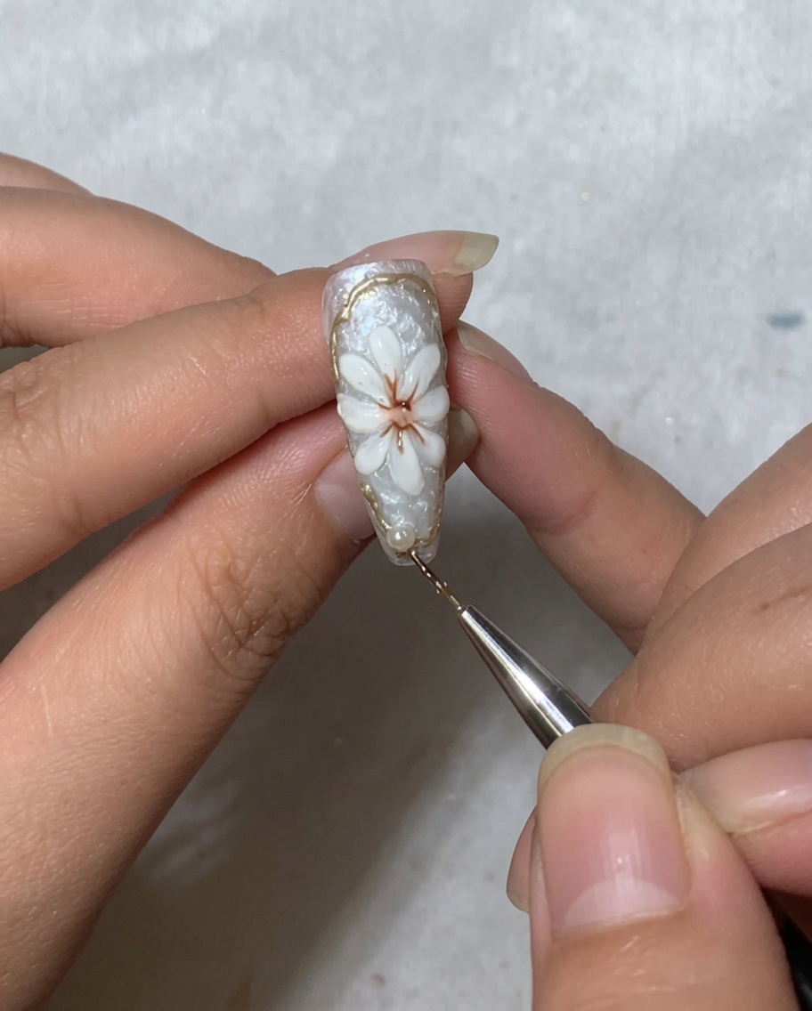 A nail art tool placing a small white pearl bead near the cuticle area of a nail decorated with a daisy.