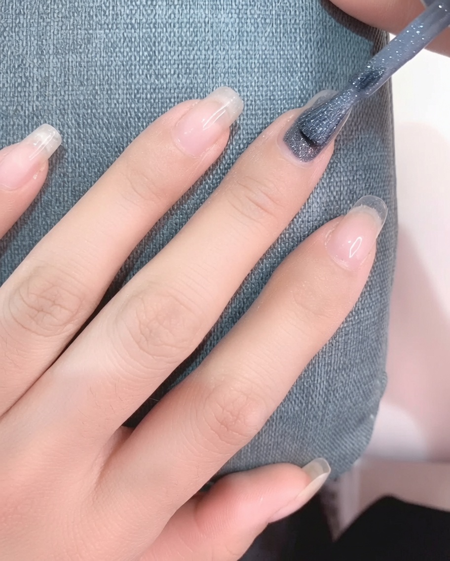 A close-up view of a brush applying light gray gel polish onto a clean fingernail.