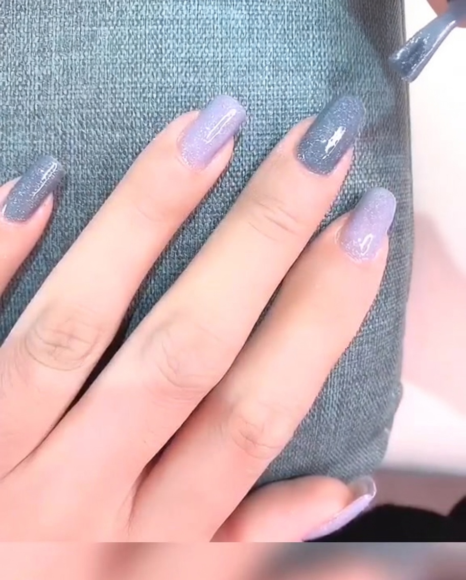 A close-up of a fingernail with two coats of gray gel polish, appearing opaque and smooth.