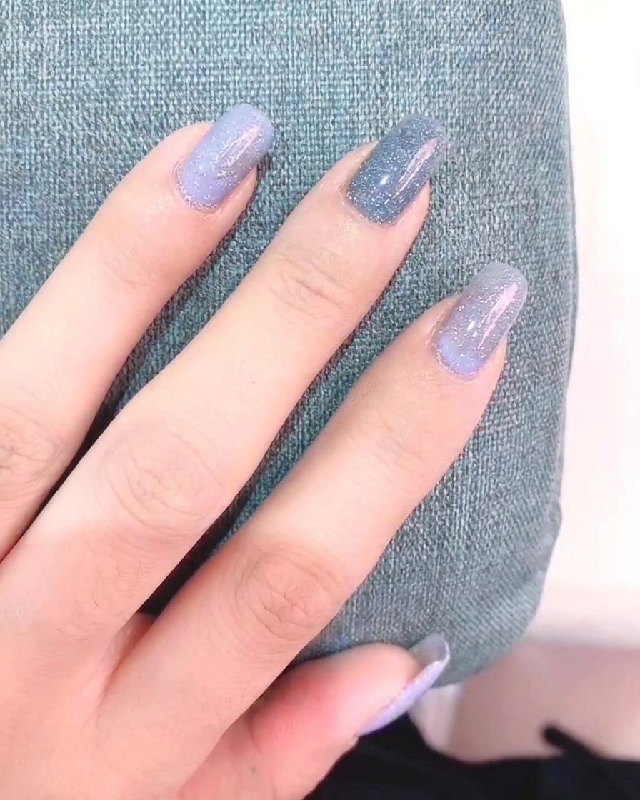 A fine liner brush held by a hand, painting white daisy petals onto a gray-painted nail.
