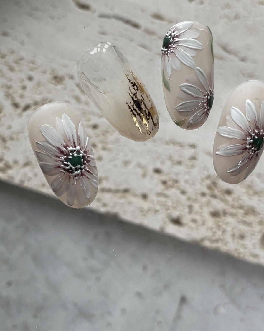 A close-up view of the nail after the fourth white petal is added to the daisy pattern.