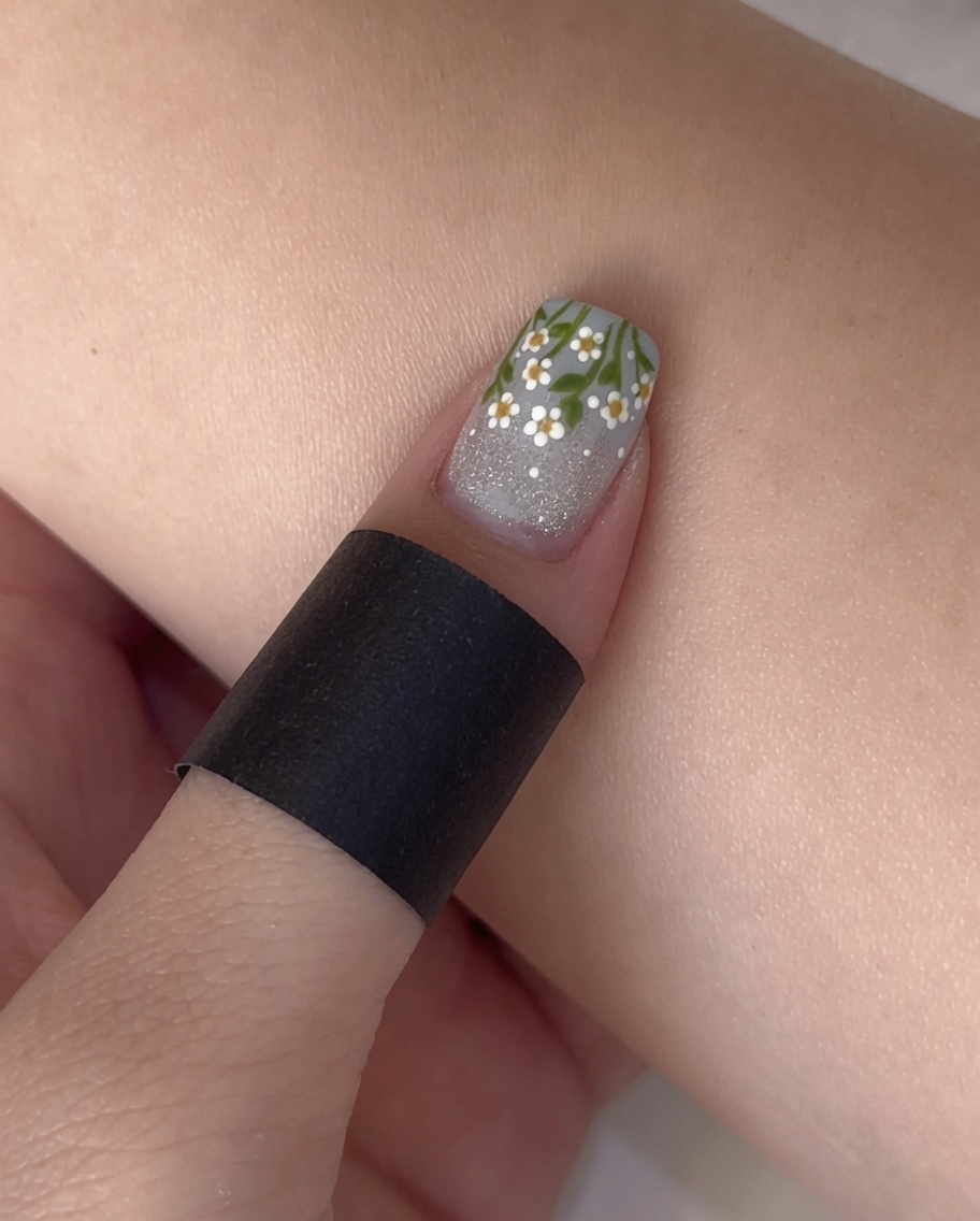 A nail polish brush applying a clear matte top coat to a nail that has a glittery cat-eye base and blue French tip.