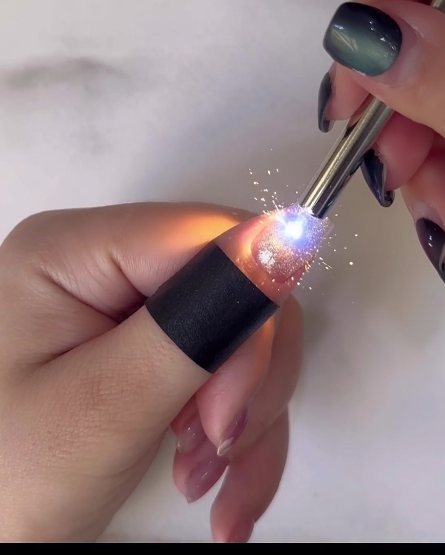 A close-up view of a dotting tool applying yellow gel to the center of a white daisy nail art design.