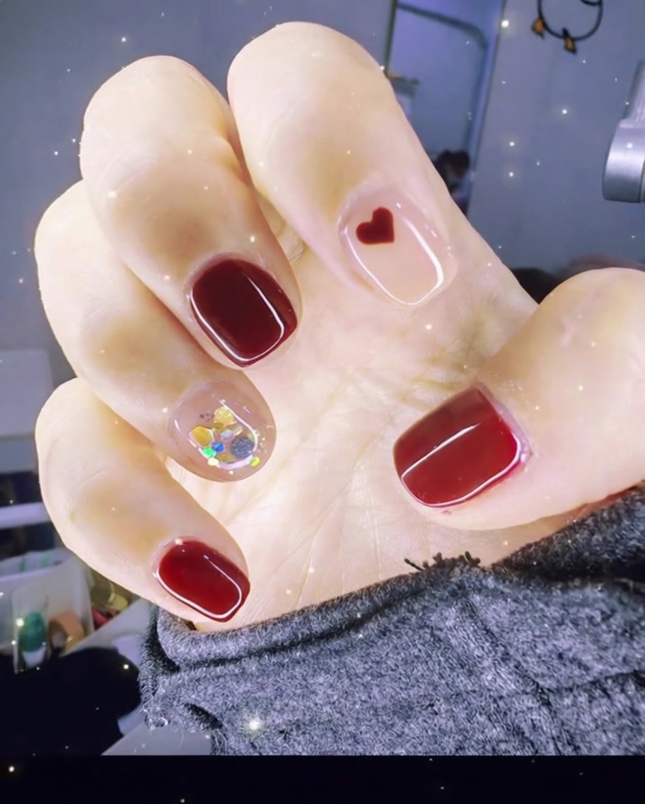 Tweezers placing a small red heart charm onto a clear gel nail surface.
