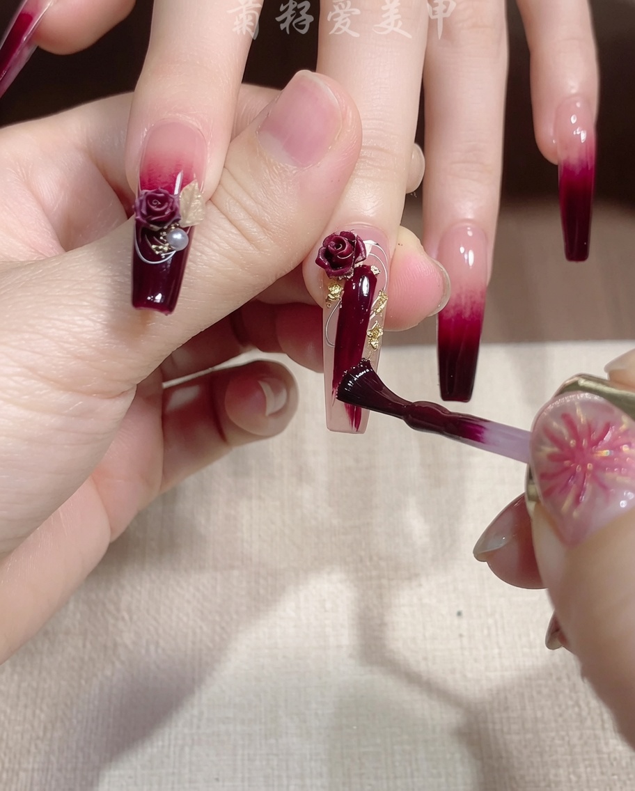 A fine brush applying a streak of sparkling gold glitter gel over a red nail.