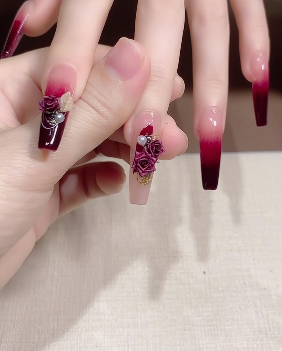 Tweezers placing a small pearl and gold decorative piece next to a rose charm on a decorated fingernail.