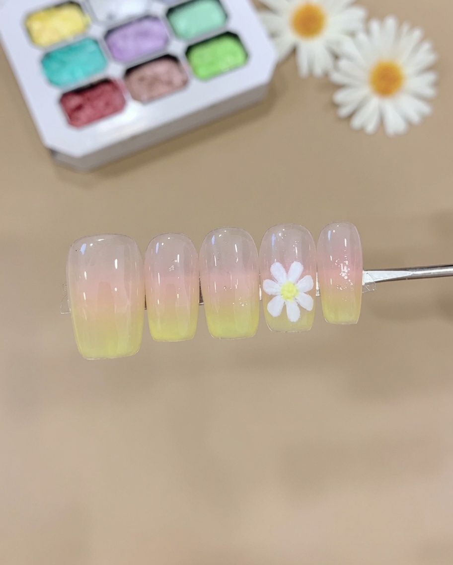 A sponge pressing pink and yellow gel onto a nail tip, creating a soft ombre gradient.