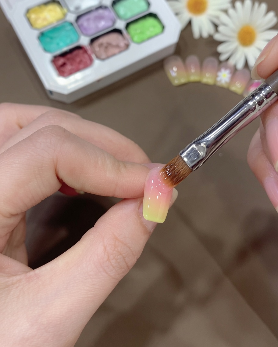 A brush carefully blending the yellow gel transition on the nail to create a smooth gradient.