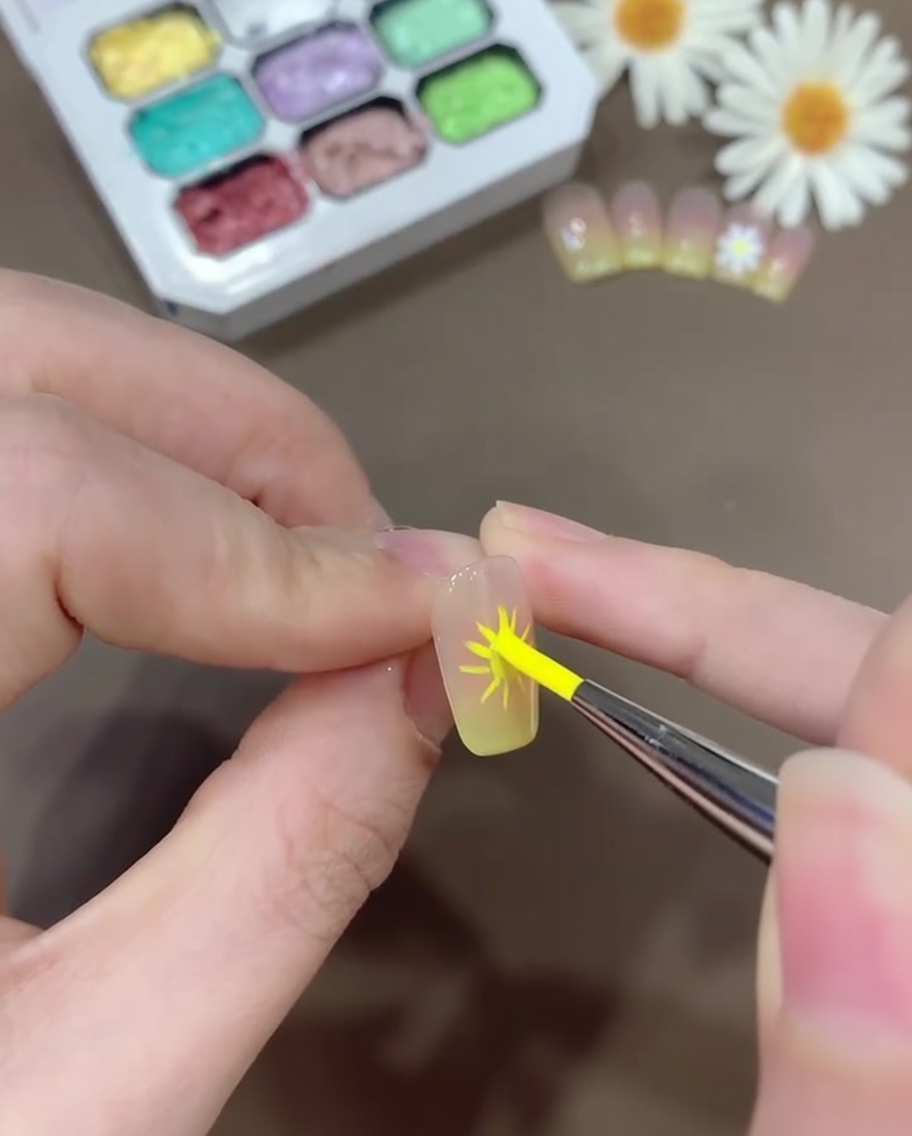 A nail art brush applying white gel to form rounded, daisy-like petals over the pre-marked petal guidelines.